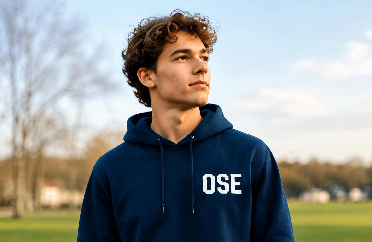Jeune ambassadeur OSE en sweat bleu, portrait authentique au bord d'un terrain de sport